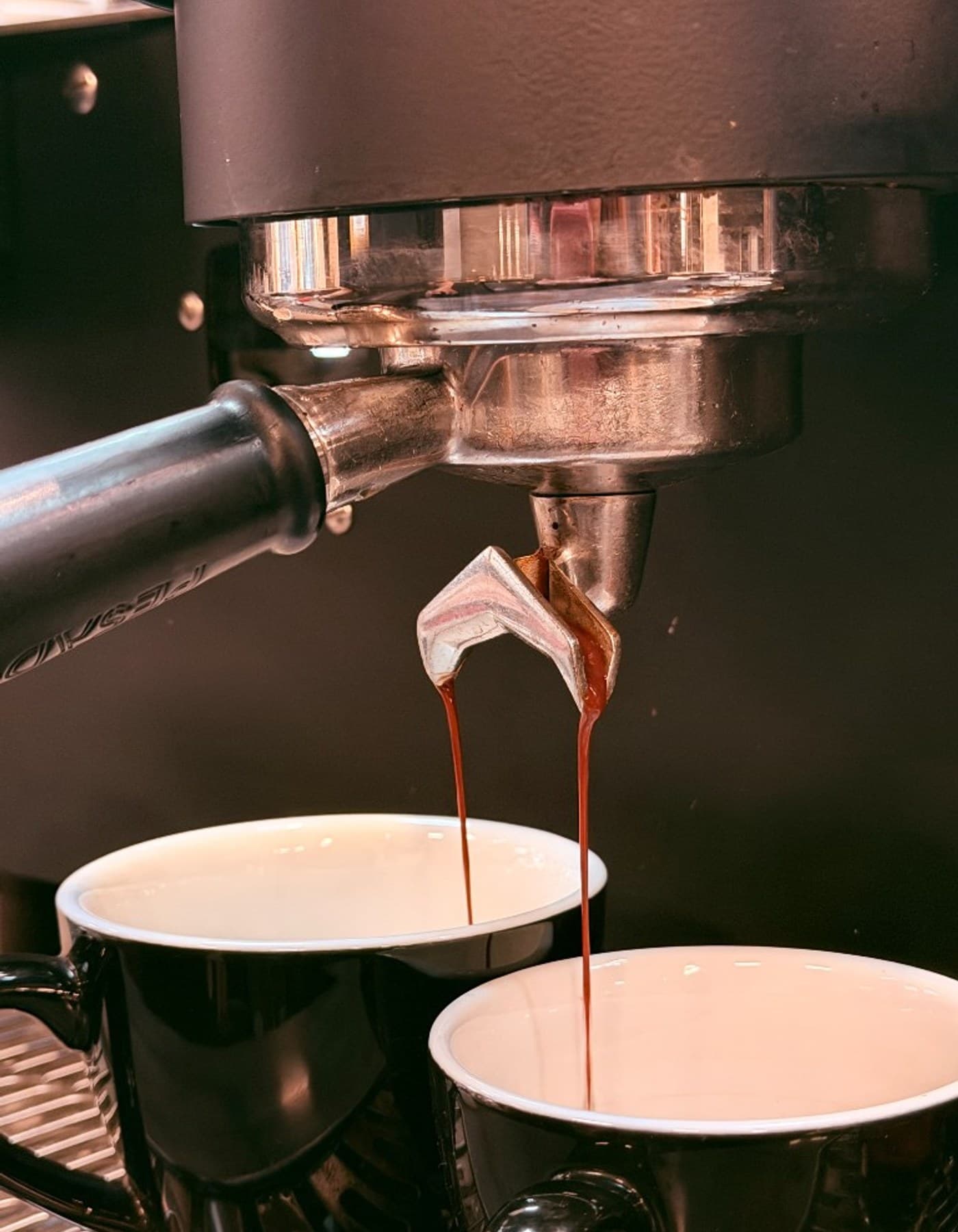 Rich espresso pouring from a portafilter into two black ceramic cups