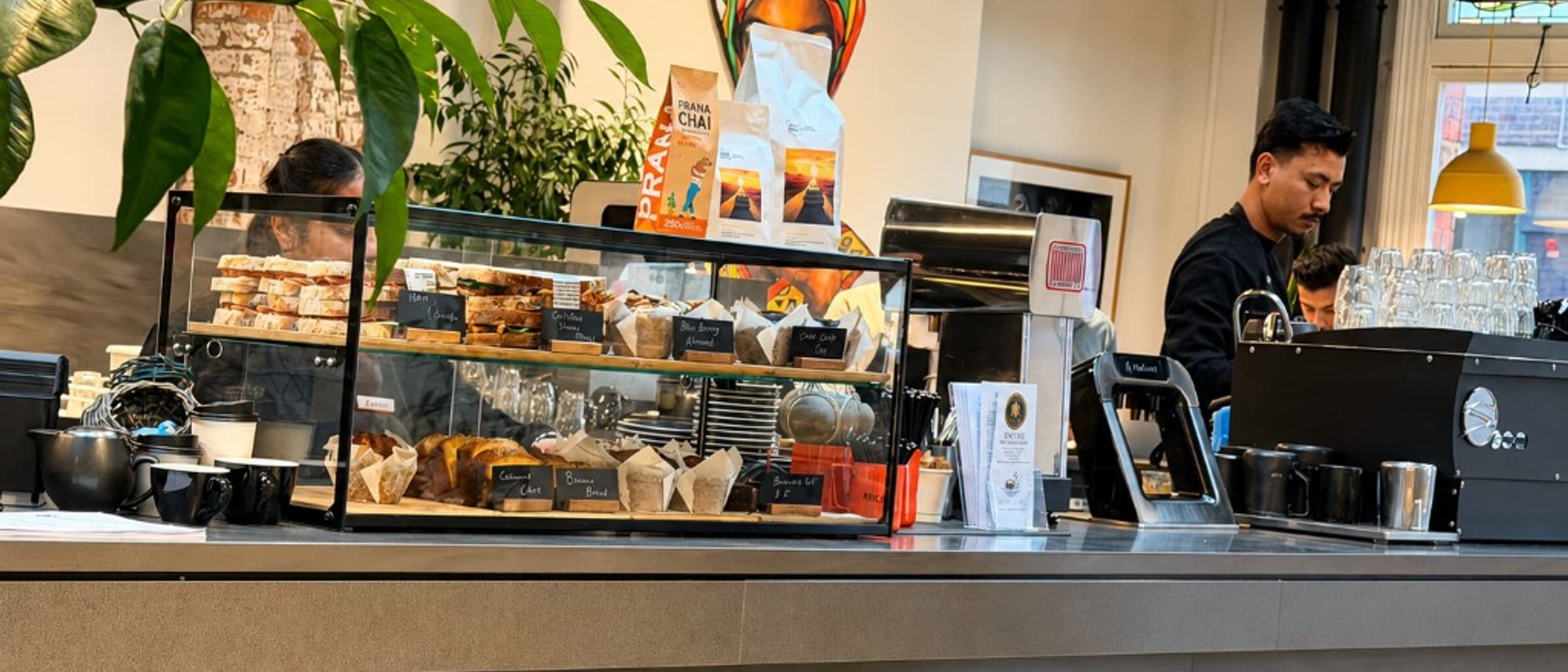 Nest Cafe counter with pastry display, coffee and a barista at the espresso machine
